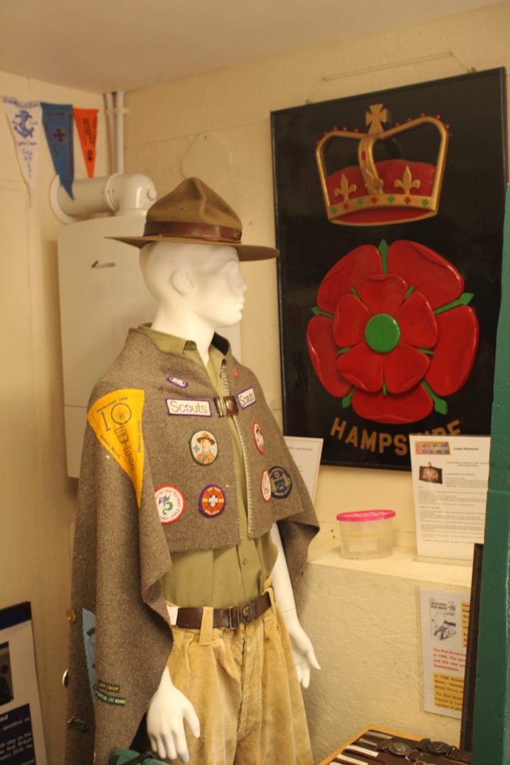 A mannequin wearing a camp blanket in front of a Hampshire Scout emblem.