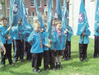 A group of Beaver Scouts holding blue flags outside.