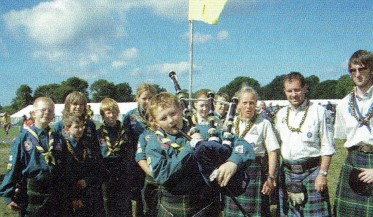 A group of Scouts from Scotland wearing uniform, kilts with one playing the bagpipes.