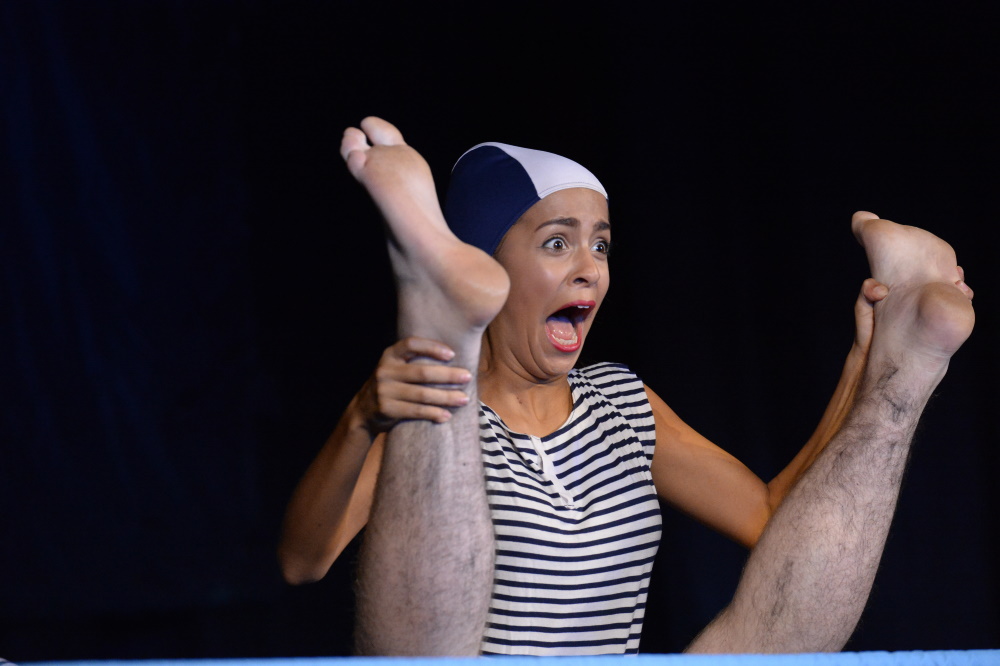 A leader performing on stage looking shocked holding an upside pair of hairy legs.